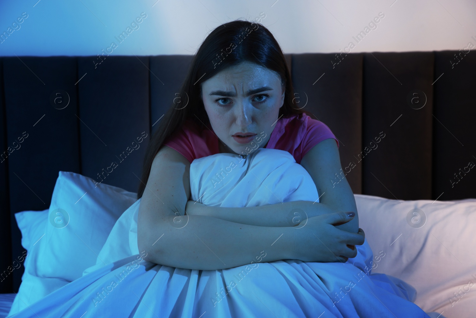 Photo of Fear of darkness. Scared young woman on bed in room at night