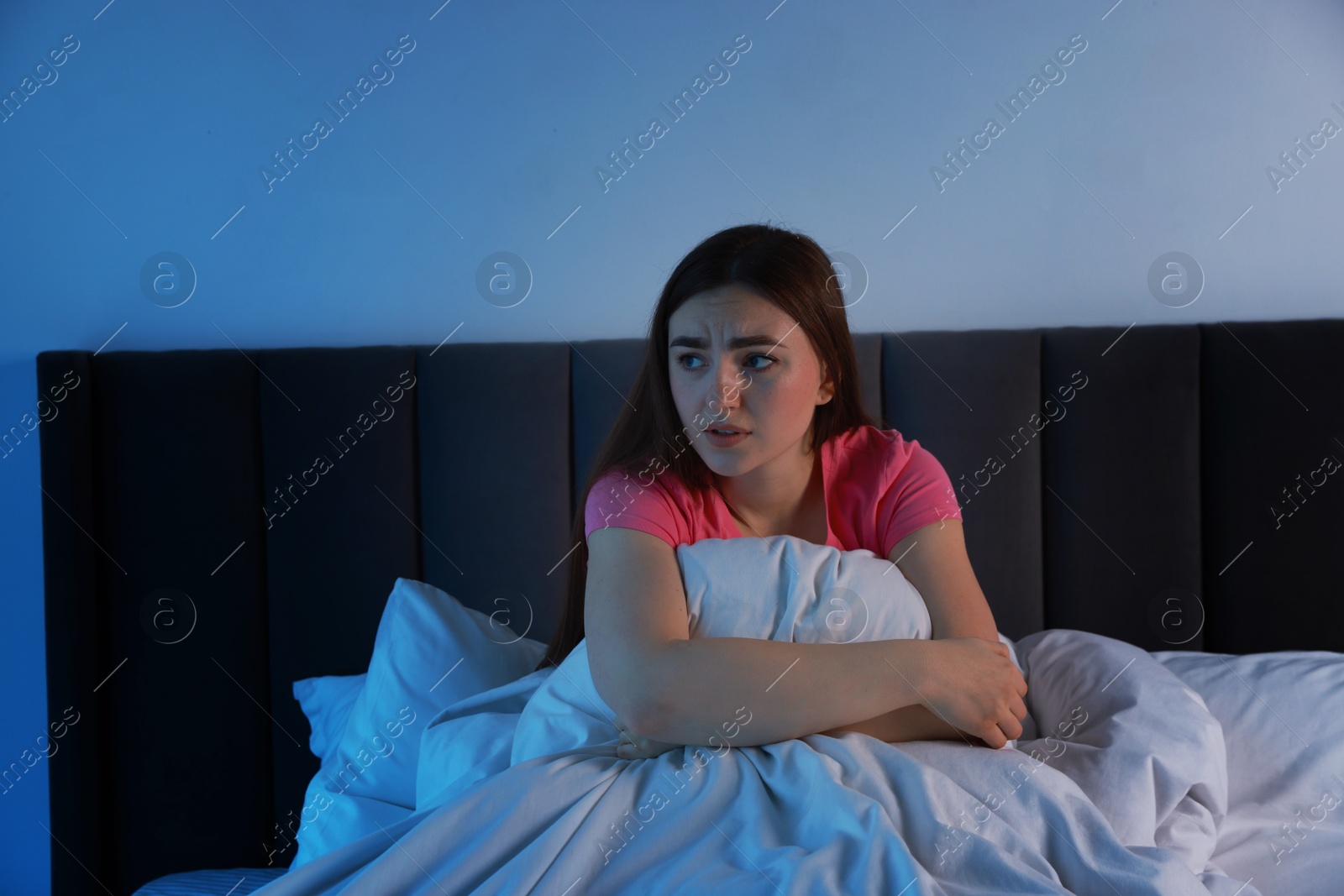 Photo of Fear of darkness. Scared young woman on bed in room at night