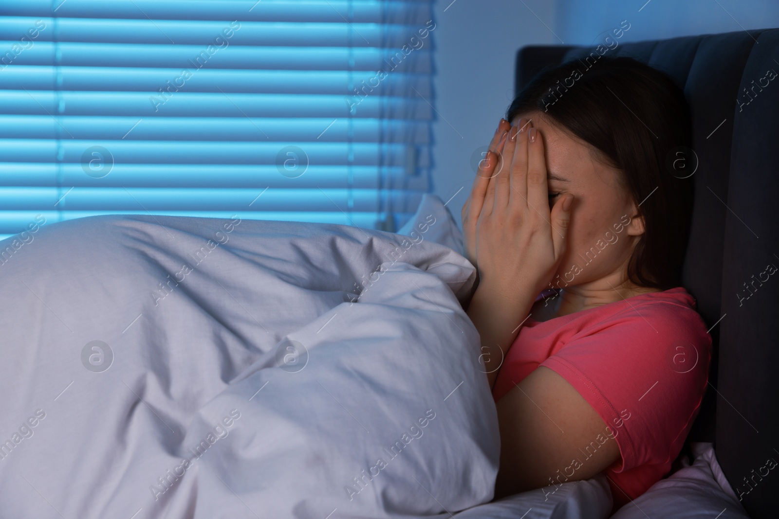 Photo of Fear of darkness. Scared young woman lying on bed in room at night, space for text