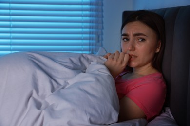 Photo of Fear of darkness. Scared young woman lying on bed in room at night, space for text