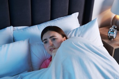 Photo of Fear of darkness. Scared young woman lying on bed in room at night