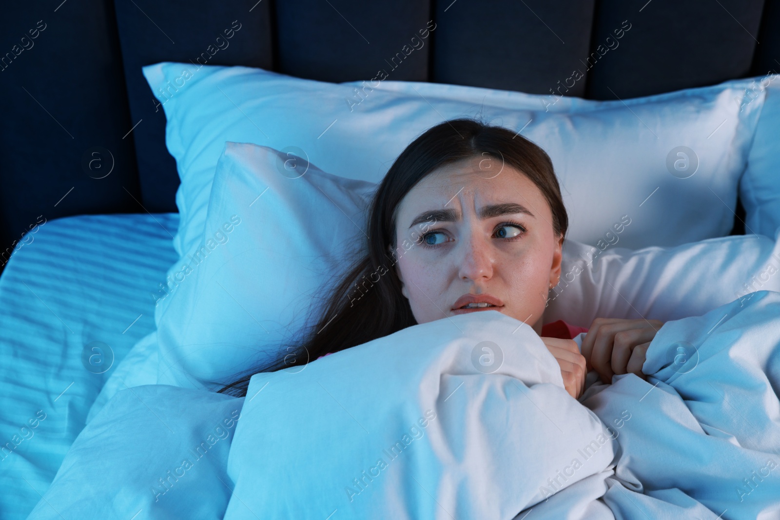 Photo of Fear of darkness. Scared young woman lying on bed in room at night