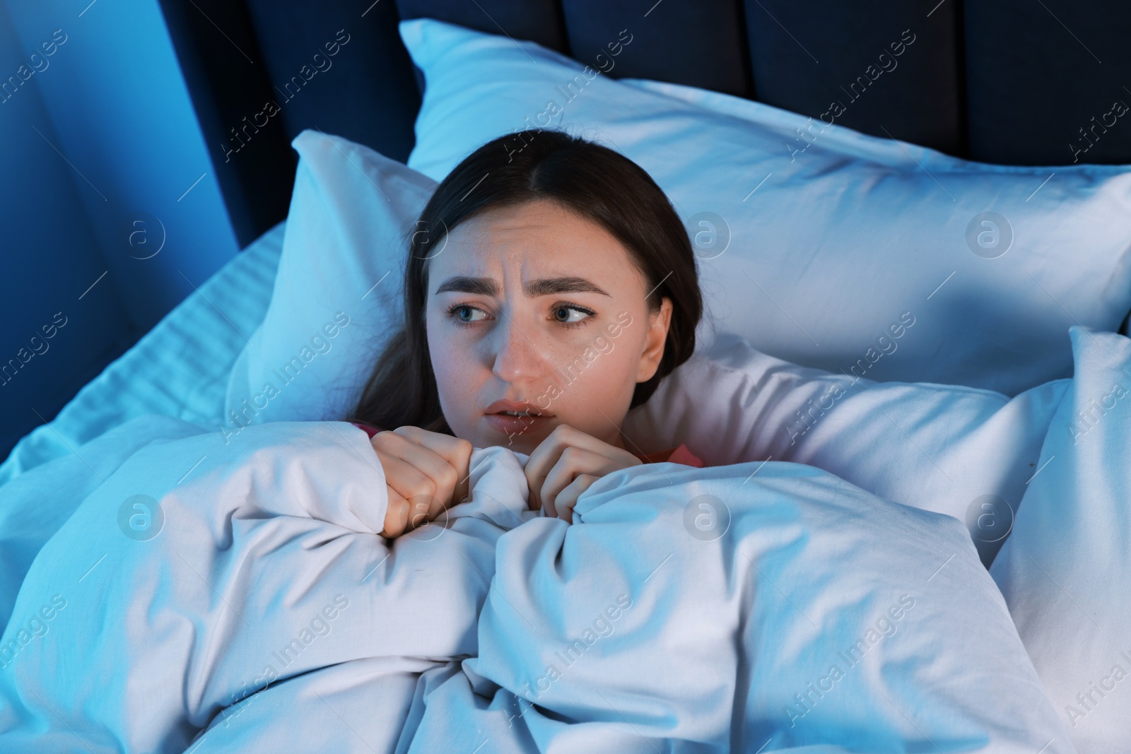 Photo of Fear of darkness. Scared young woman lying on bed in room at night