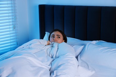 Photo of Fear of darkness. Scared young woman lying on bed in room at night