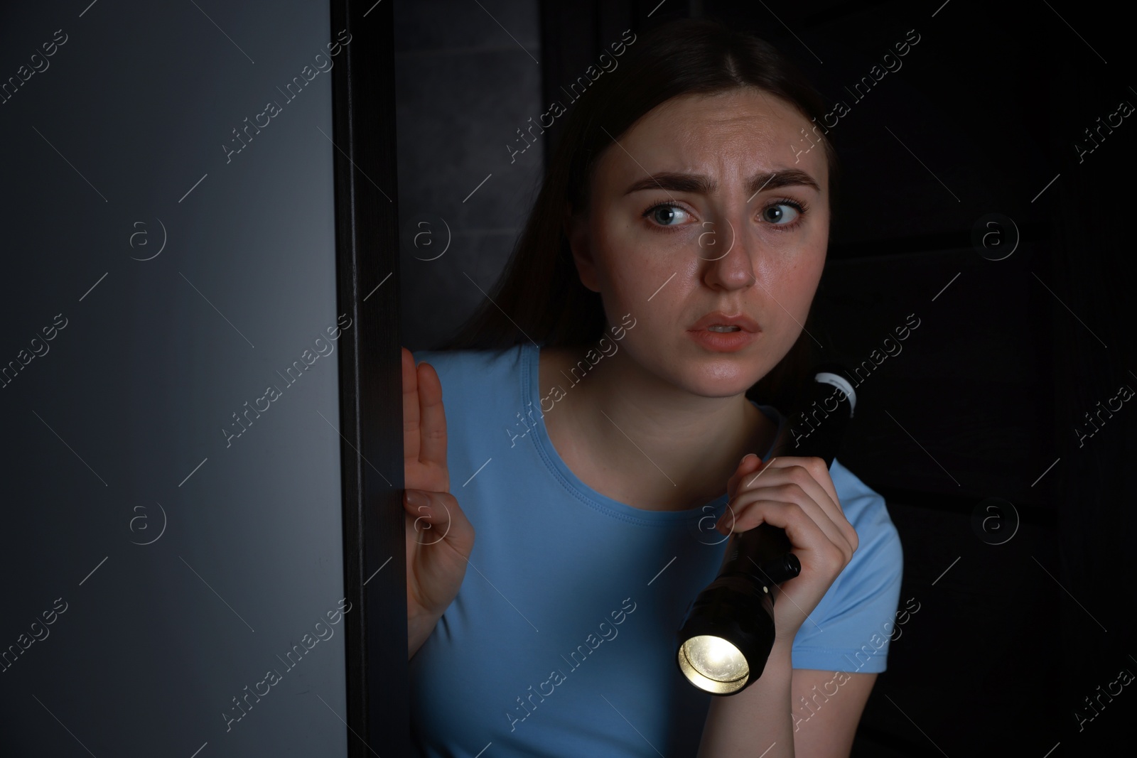 Photo of Fear of darkness. Scared young woman with flashlight indoors at night