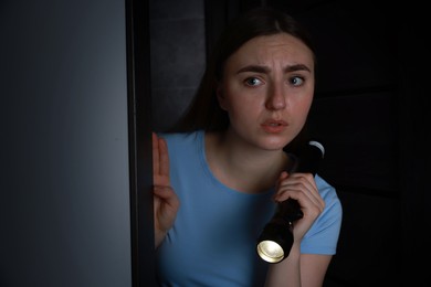 Photo of Fear of darkness. Scared young woman with flashlight indoors at night