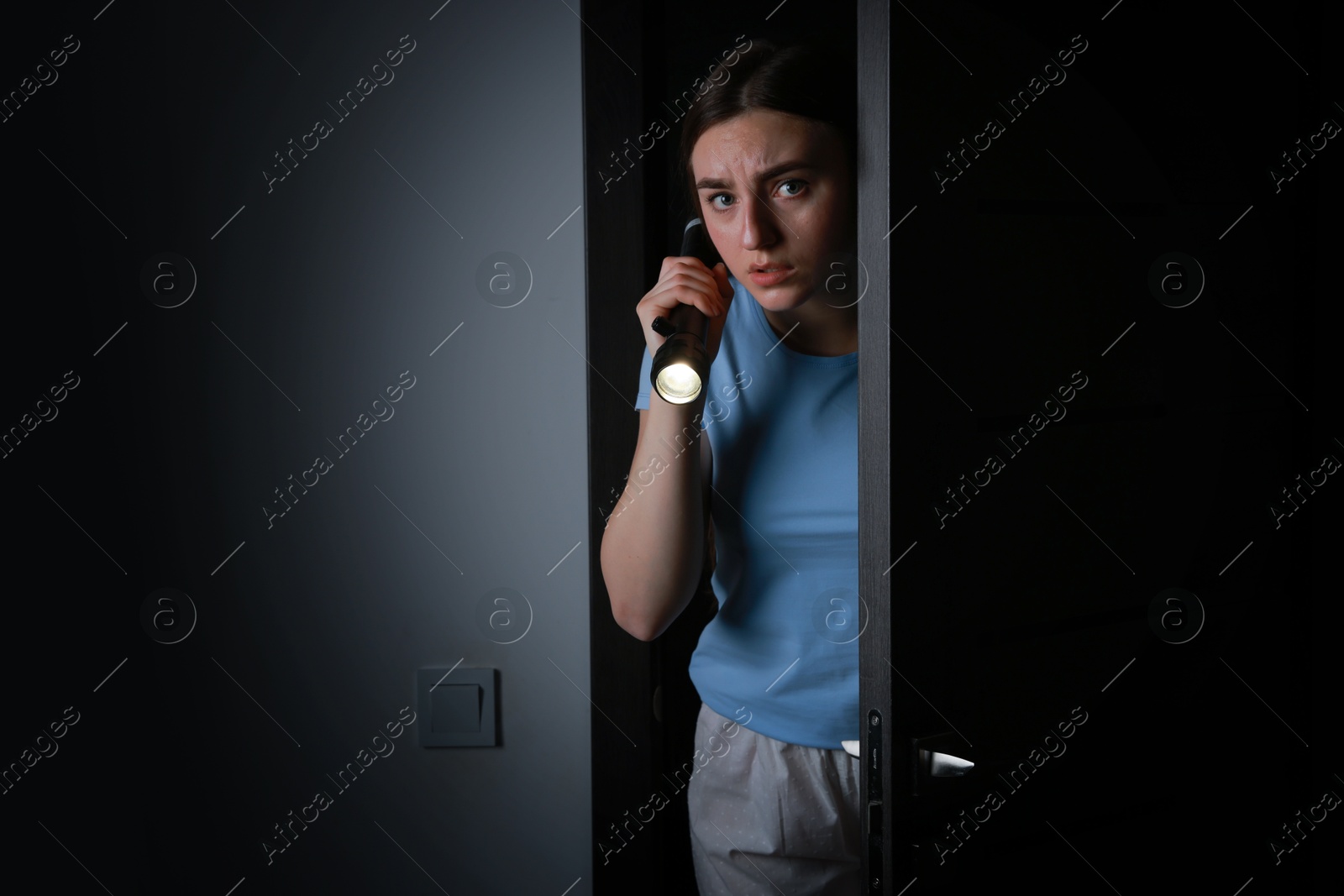 Photo of Fear of darkness. Scared young woman with flashlight indoors at night