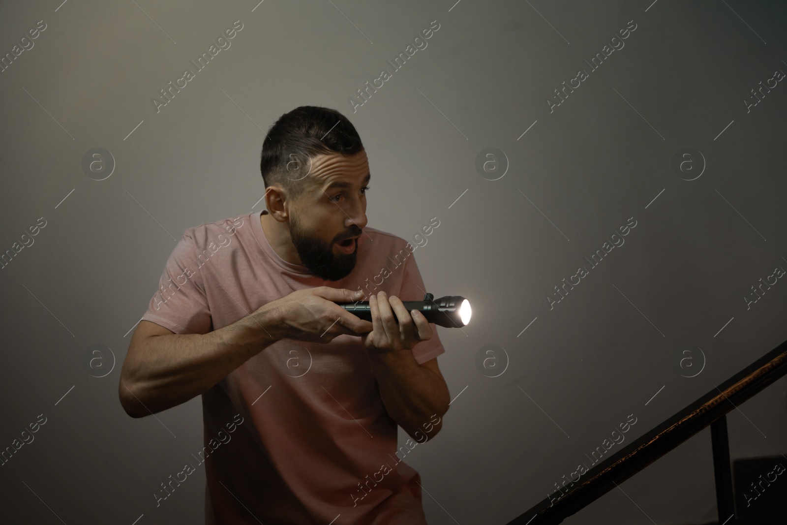 Photo of Fear of darkness. Scared man with flashlight indoors at night, space for text