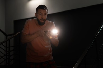 Photo of Fear of darkness. Scared man with flashlight indoors at night