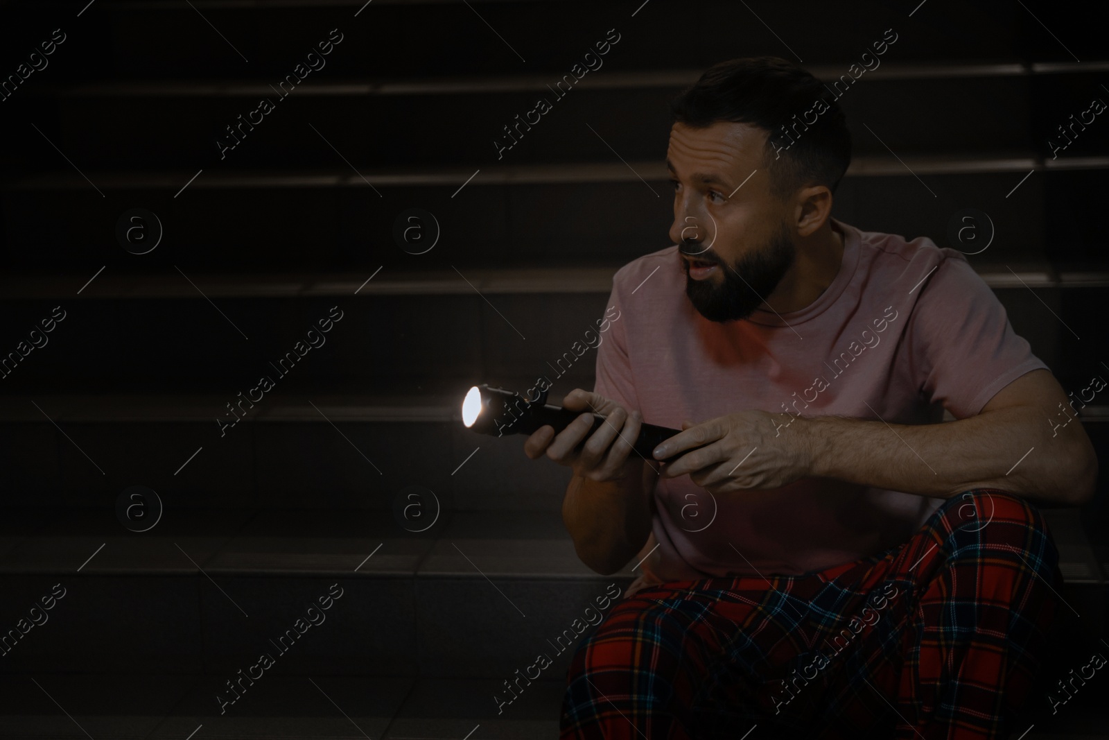 Photo of Fear of darkness. Scared man with flashlight indoors at night, space for text