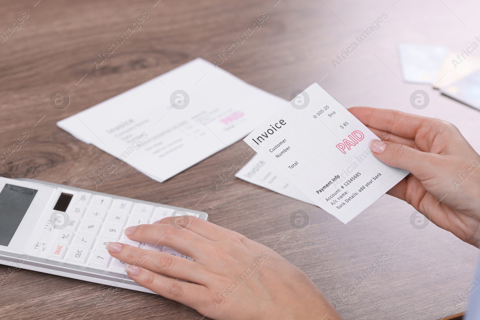 Photo of Paying bills. Woman with different invoices and calculator at wooden table indoors, closeup