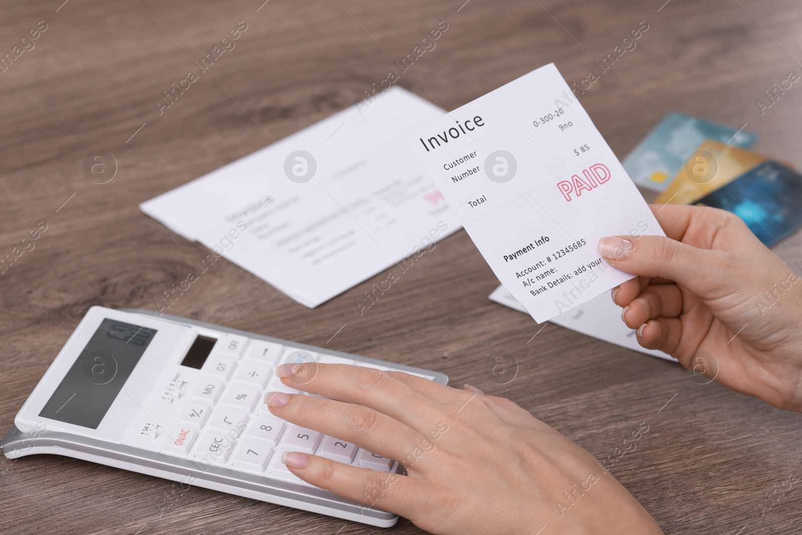 Photo of Paying bills. Woman with different invoices and calculator at wooden table indoors, closeup