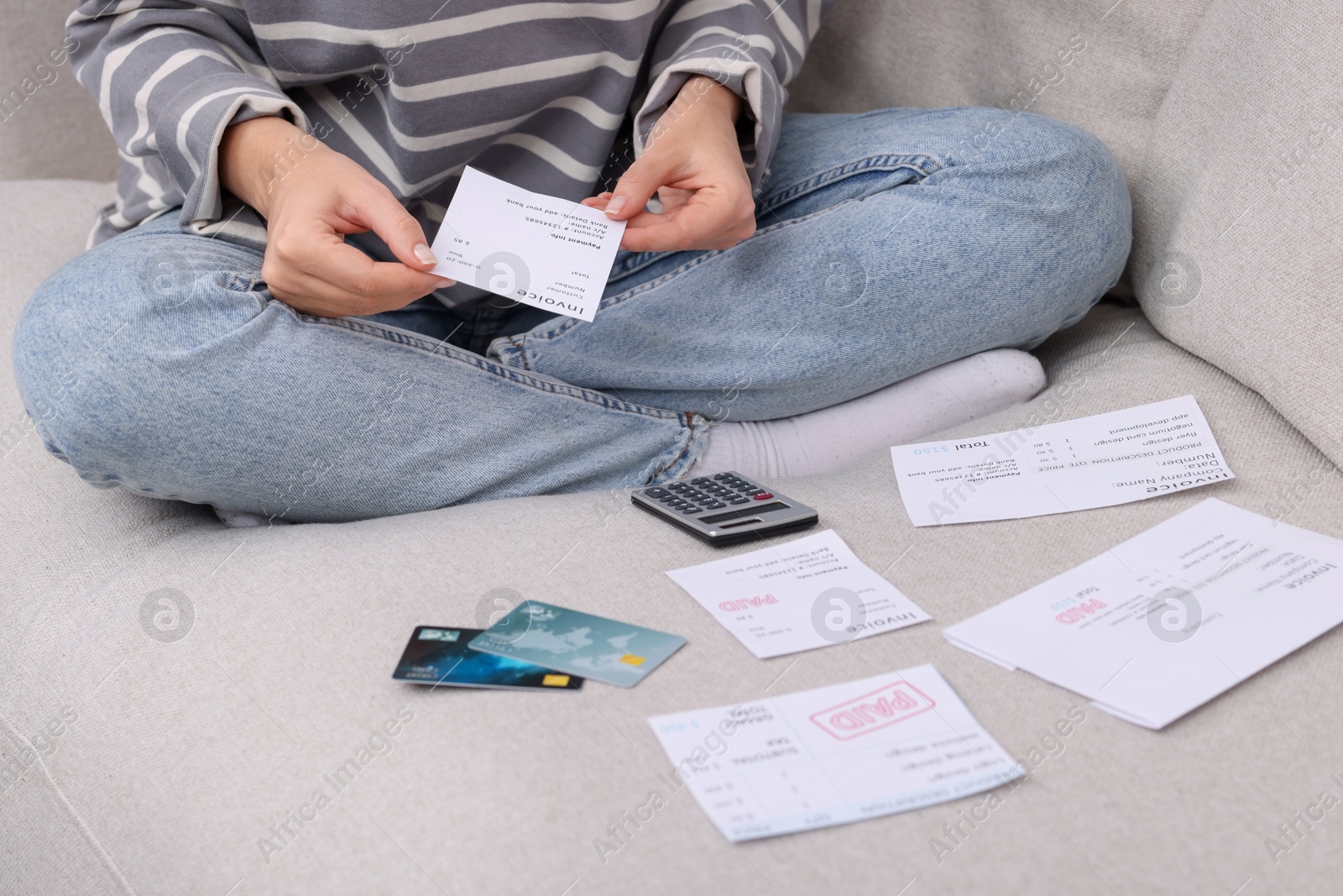 Photo of Paying bills. Woman with different invoices, credit cards and calculator on couch at home, closeup