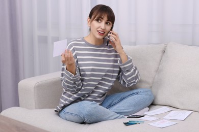 Photo of Paying bills. Woman with different invoices talking on phone on couch at home