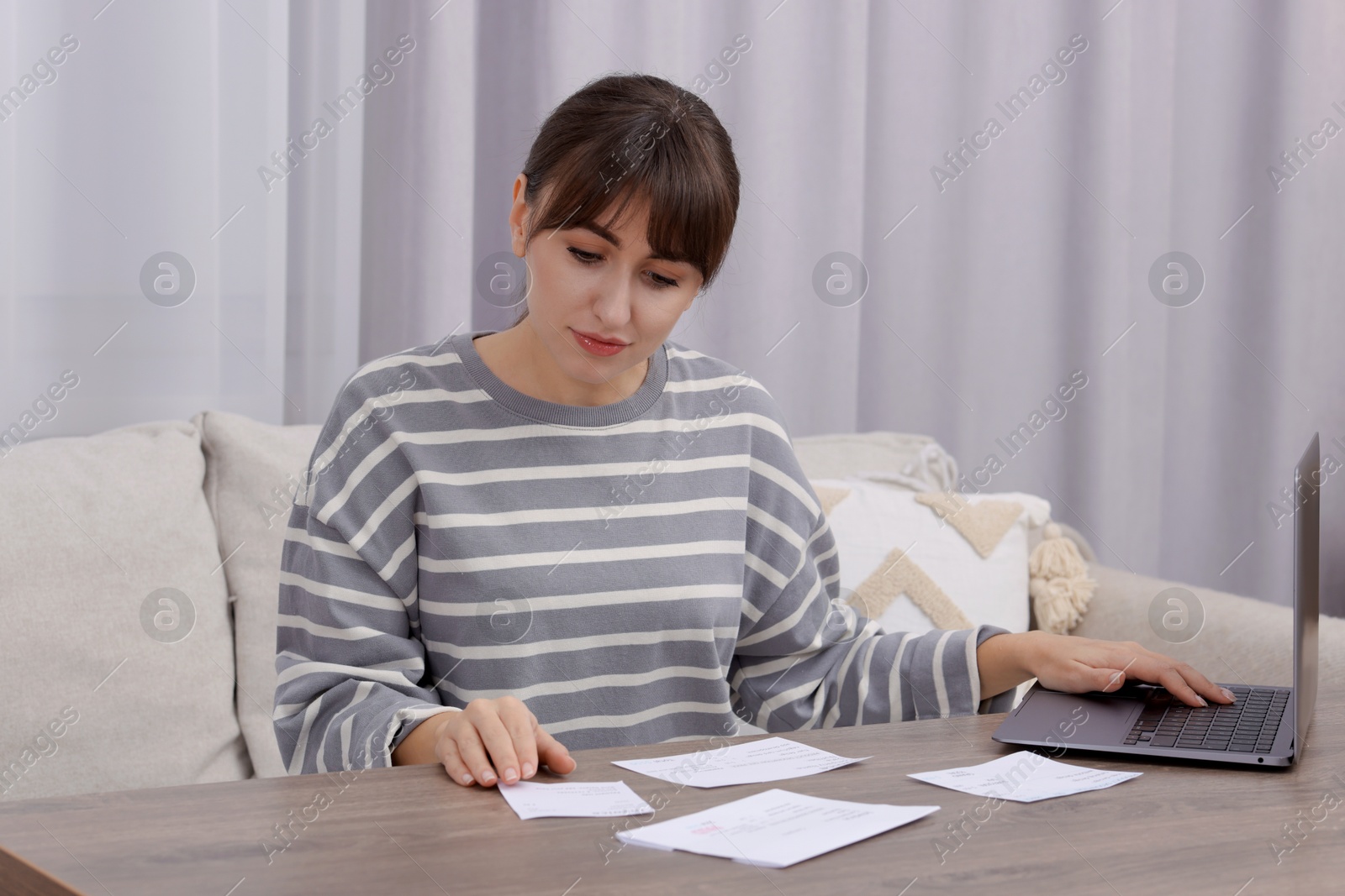 Photo of Paying bills. Woman with different invoices and laptop at wooden table indoors