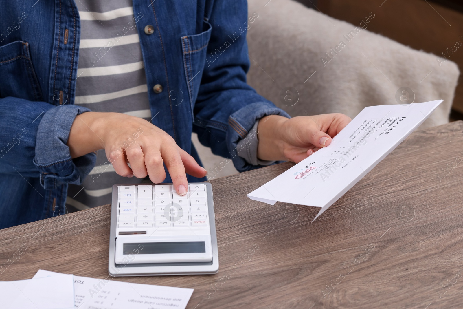 Photo of Paying bills. Woman with different invoices and calculator at wooden table indoors, closeup