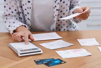 Photo of Paying bills. Woman with different invoices, credit cards and calculator at wooden table indoors, closeup