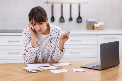 Photo of Paying bills. Upset woman with different invoices and calculator at wooden table indoors