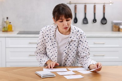 Photo of Paying bills. Woman with different invoices and calculator at wooden table indoors