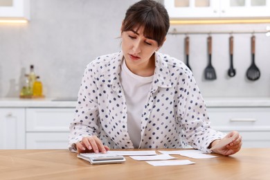 Photo of Paying bills. Woman with different invoices and calculator at wooden table indoors