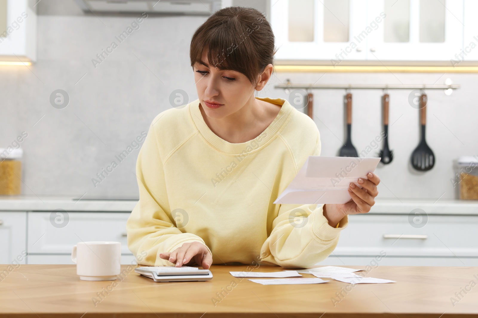 Photo of Paying bills. Woman with different invoices and calculator at wooden table indoors