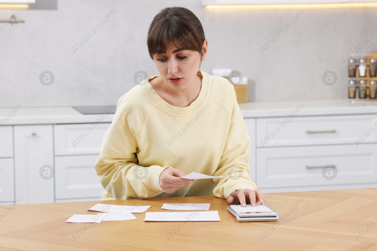 Photo of Paying bills. Woman with different invoices and calculator at wooden table indoors