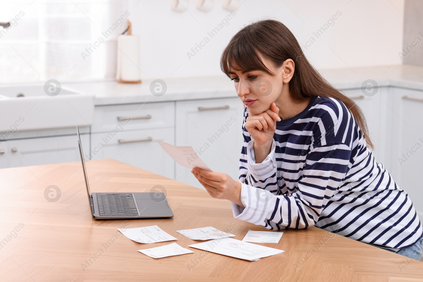 Photo of Paying bills. Woman with different invoices and laptop at wooden table indoors