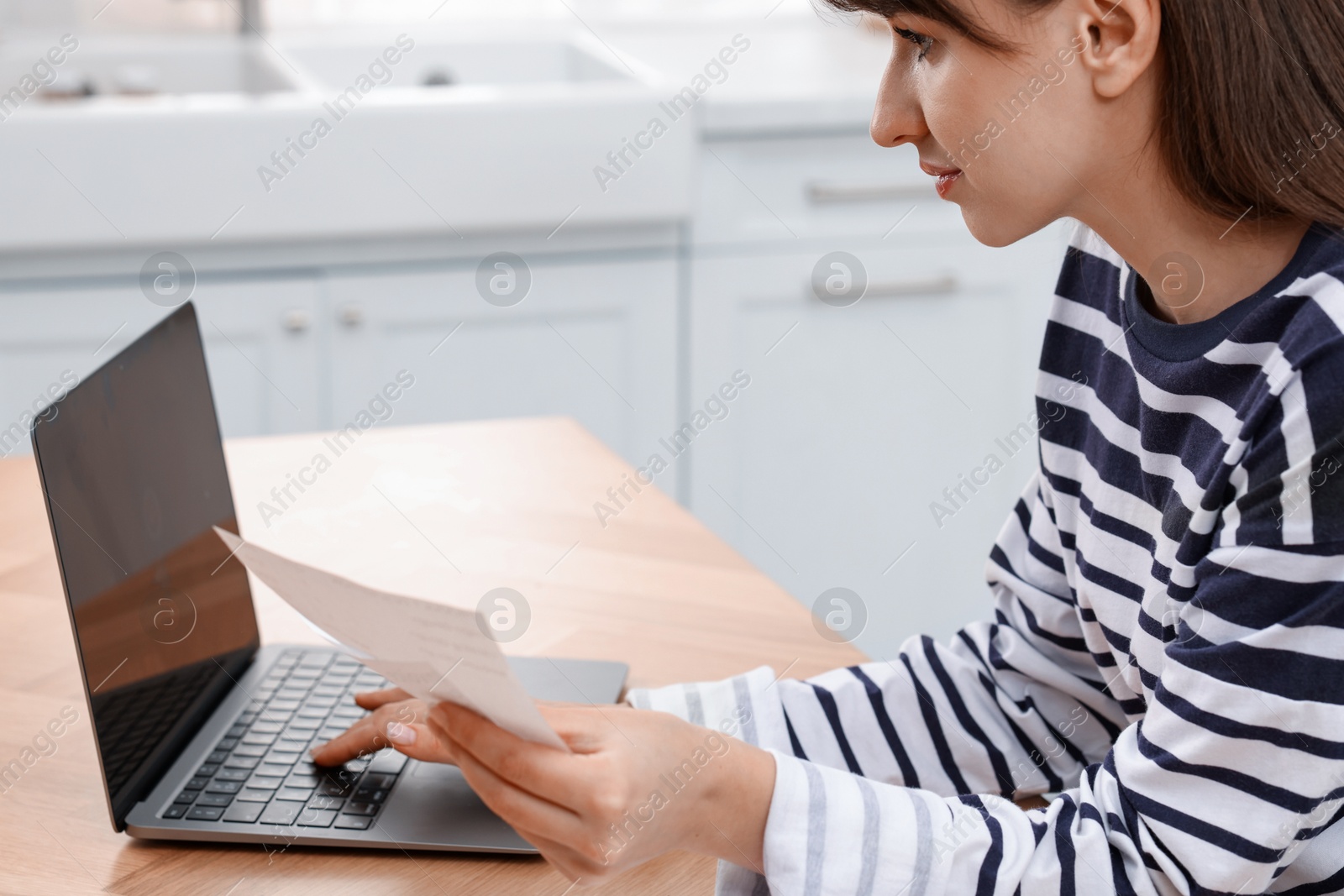 Photo of Paying bills. Woman with different invoices and laptop at wooden table indoors, closeup