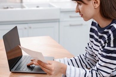 Photo of Paying bills. Woman with different invoices and laptop at wooden table indoors, closeup