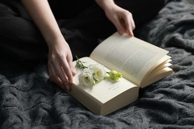 Photo of Woman reading book with beautiful flowers on blanket, closeup