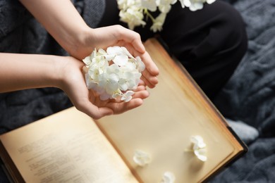 Woman holding pile of flower buds above book on blanket, top view