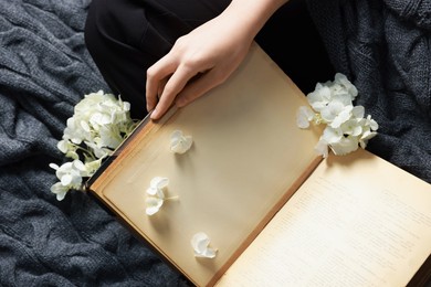 Photo of Woman reading book with beautiful flowers on blanket, top view