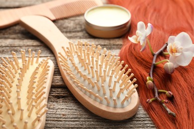 Photo of Brushes, wax, orchid branch and lock of hair on wooden table, closeup