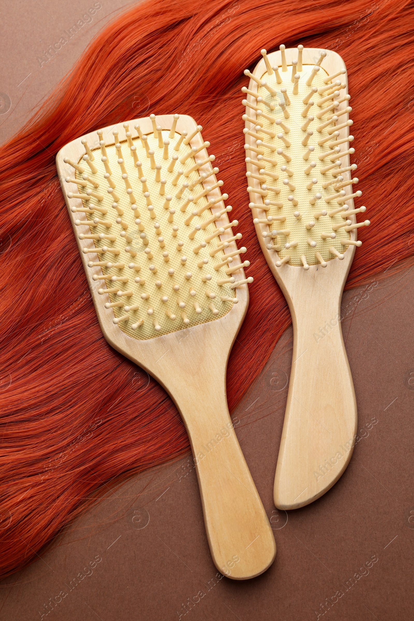 Photo of Brushes and lock of hair on brown background, flat lay