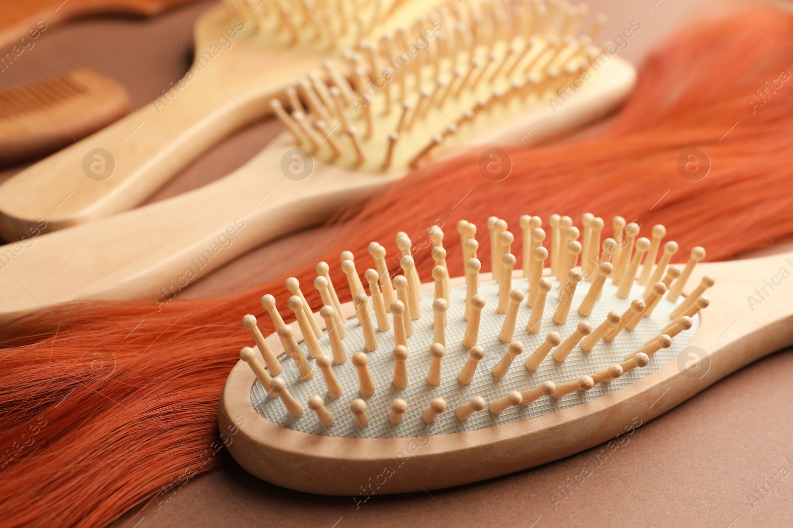 Photo of Wooden brushes and lock of hair on brown background, closeup