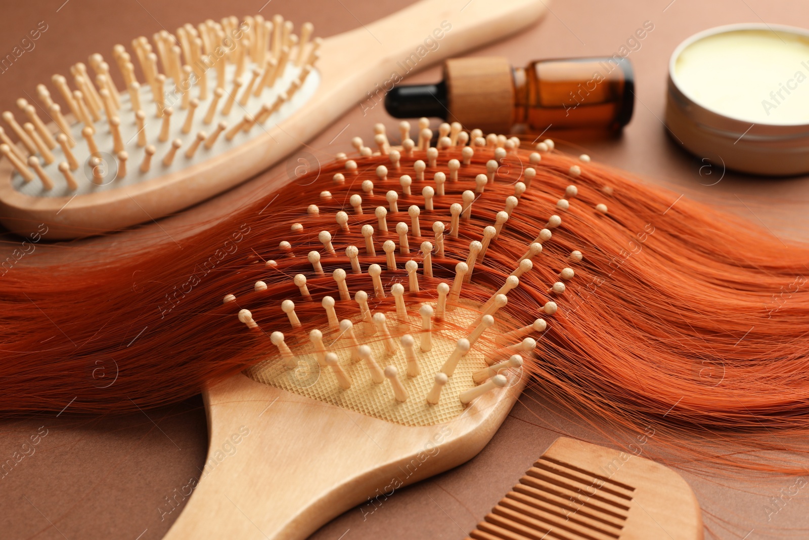 Photo of Wooden brushes, comb and lock of hair on brown background, closeup