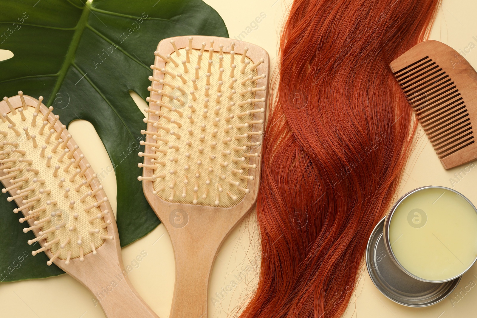 Photo of Wooden brushes, wax, comb, lock of hair and monstera leaf on beige background, flat lay