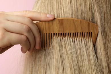 Photo of Woman brushing hair with wooden comb on pink background, closeup