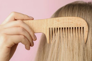 Photo of Woman brushing hair with wooden comb on pink background, closeup