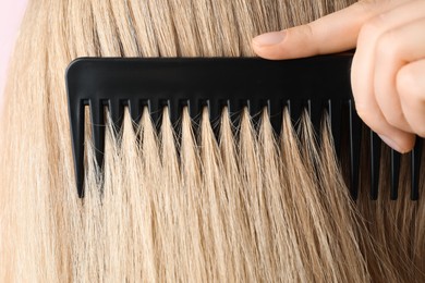 Photo of Woman brushing hair with plastic comb on pink background, closeup