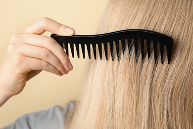 Photo of Woman brushing hair with plastic comb on beige background, closeup