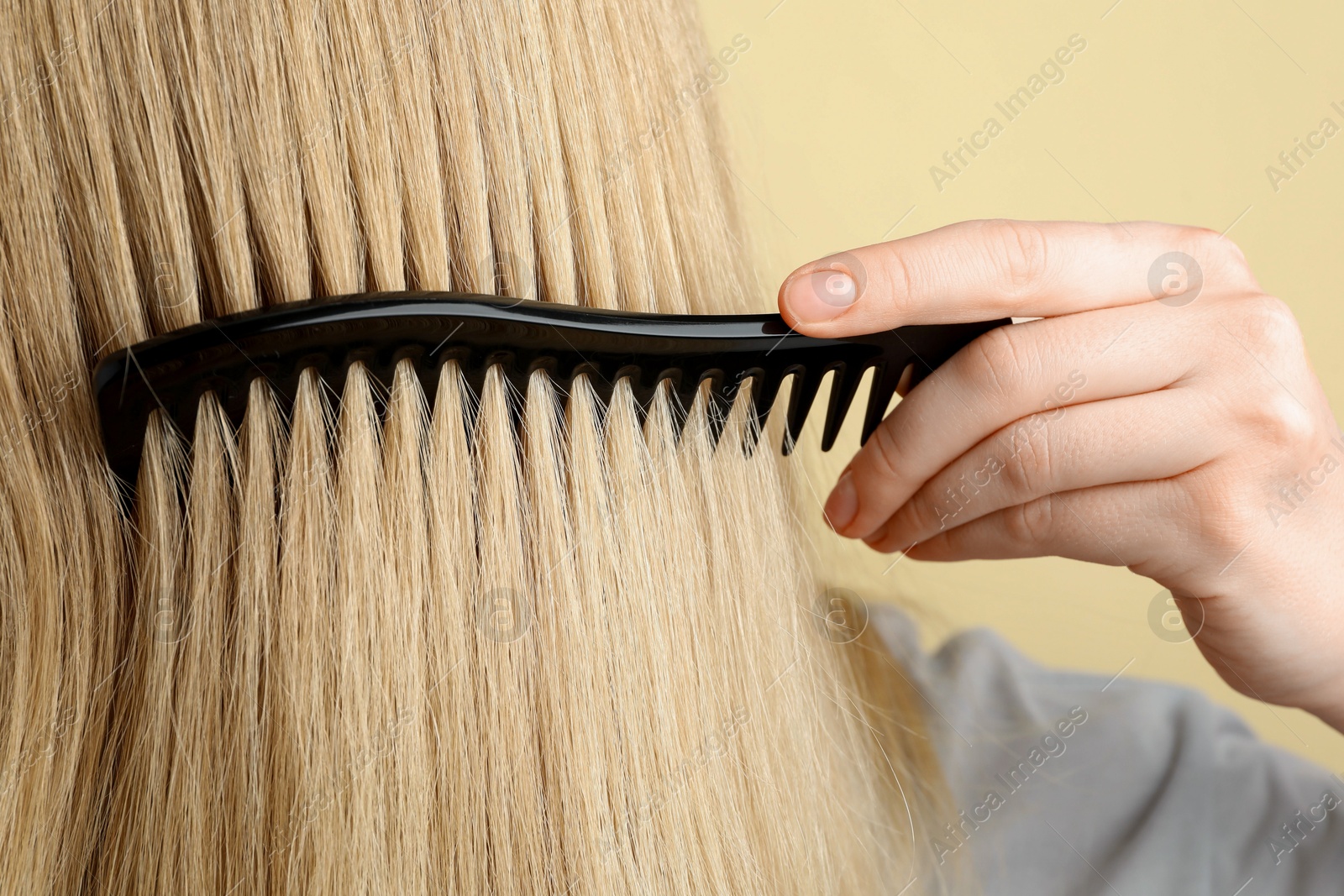 Photo of Woman brushing hair with plastic comb on beige background, closeup