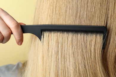 Photo of Woman brushing hair with plastic comb on beige background, closeup