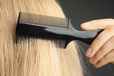 Photo of Woman brushing hair with plastic comb on grey background, closeup