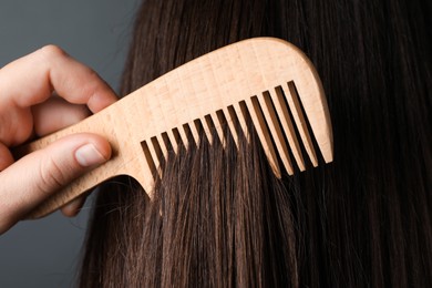 Photo of Woman brushing hair with wooden comb on grey background, closeup