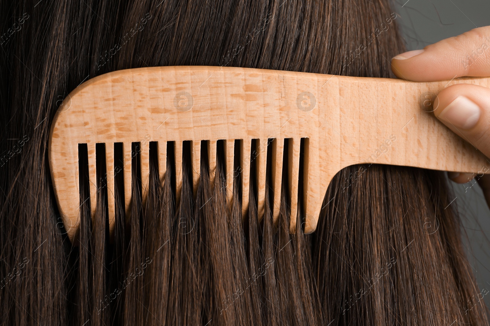 Photo of Woman brushing hair with wooden comb on grey background, closeup