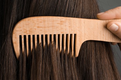 Photo of Woman brushing hair with wooden comb on grey background, closeup