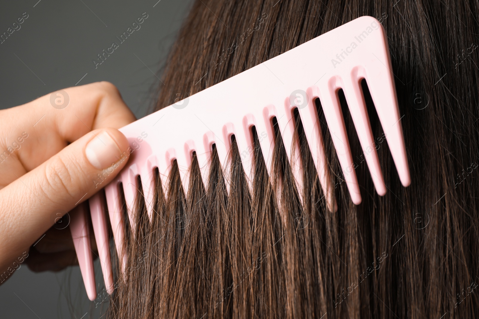 Photo of Woman brushing hair with plastic comb on grey background, closeup