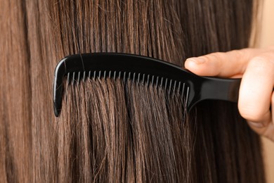 Photo of Woman brushing hair with plastic comb, closeup