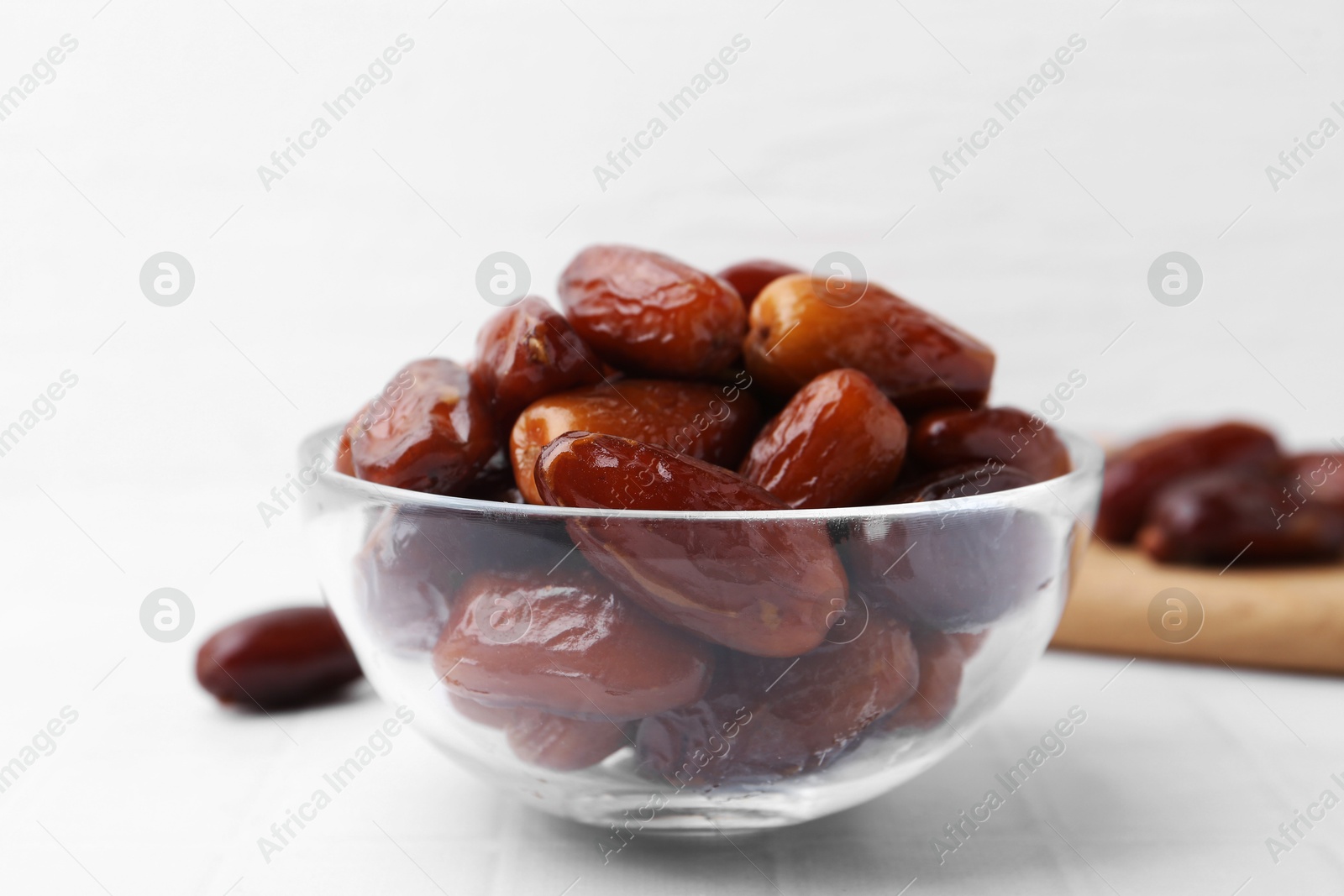 Photo of Tasty dried dates in glass bowl on white table, closeup